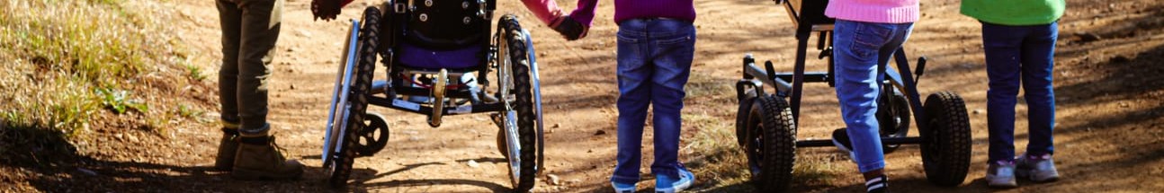 five children walking down a road together, two are using wheelchairs